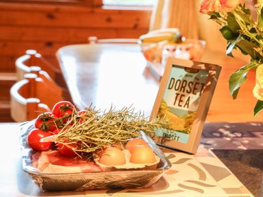 A kitchen table with tomatoes, eggs, herbs, and a framed Dorset Tea sign at Rose Lodge in Milton on Stour