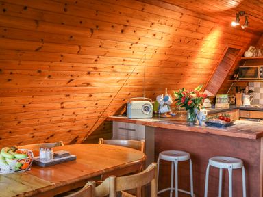 A wooden kitchen with a breakfast bar stools flowers and a dining table with fruit at Rose Lodge in Milton on Stour