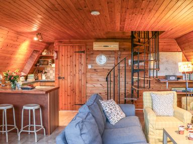 A wooden interior room with a kitchen island and stools a blue sofa a yellow armchair a spiral staircase and a wooden door at Rose Lodge in Milton on Stour