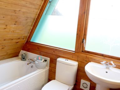 A bathroom with a bathtub beside a toilet and a pedestal sink under a large frosted window at Rose Lodge in Milton on Stour