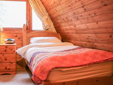 A bedroom with a wooden bed covered with a colorful blanket and a nightstand with a radio at Rose Lodge in Milton on Stour