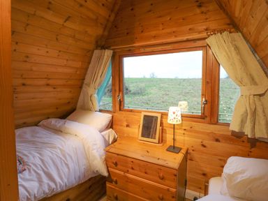 A wooden bedroom with a bed a dresser a lamp and a large window at Rose Lodge in Milton on Stour