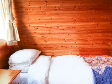 A bedroom with a single bed with white pillows and bedding next to a window with curtains and wooden walls at Rose Lodge in Milton on Stour