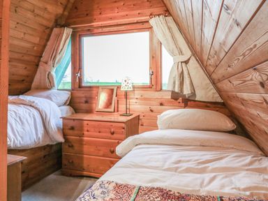 A bedroom with two single beds wooden walls a window and a chest of drawers at Rose Lodge in Milton on Stour