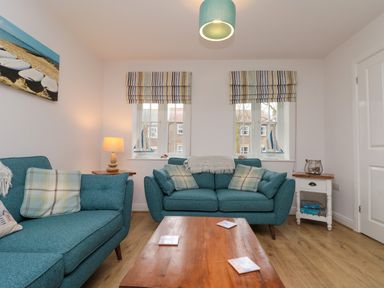 A living room with two teal sofas a wooden coffee table and two windows with striped roman blinds at Dotty's Sunshine Cottage in The Bay near Filey