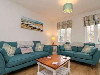 A living room with two teal sofas a wooden coffee table a table lamp and wall art of boats at Dotty's Sunshine Cottage The Bay near Filey