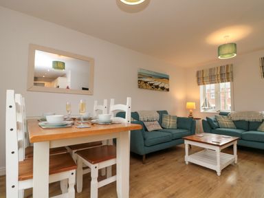 An open plan living and dining area with a wooden dining table and chairs two teal sofas a wooden coffee table and a wall mirror at Dotty's Sunshine Cottage in The Bay near Filey