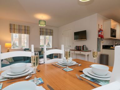 A dining table set with plates bowls cutlery and glasses in an open plan living and kitchen area at Dotty's Sunshine Cottage The Bay near Filey