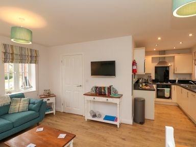 A living room with a teal sofa a wooden coffee table and a white cabinet with books and a TV mounted above at Dotty's Sunshine Cottage in The Bay near Filey