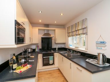 A kitchen with black countertops white cabinets a built in oven a gas stove a stainless steel kettle a dish drainer and a window with a striped blind at Dotty's Sunshine Cottage The Bay near Filey