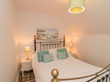 A bedroom with a metal bed frame two bedside tables with lamps and a beach painting on the wall at Dotty's Sunshine Cottage in The Bay near Filey