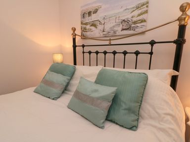 A bedroom with a metal bedframe three green cushions and a lamp at Dotty's Sunshine Cottage in The Bay near Filey