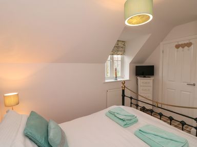 A bedroom with a bed towels cushions a lamp a small dresser with a television and a window at Dotty's Sunshine Cottage The Bay near Filey