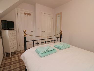 A bedroom with a bed with folded towels a chest of drawers with a TV two doors and a wall mirror at Dotty's Sunshine Cottage The Bay near Filey