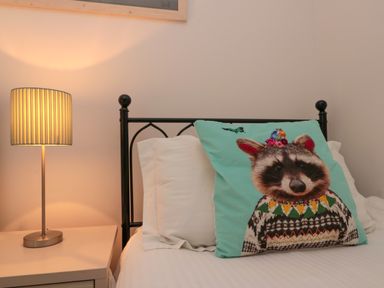 A bed with white pillows and a pillow with a raccoon design next to a bedside table with a lit lamp at Dotty's Sunshine Cottage The Bay near Filey