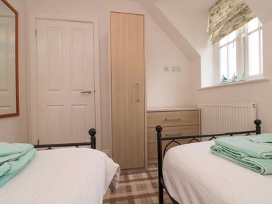 A bedroom with two single beds a wooden wardrobe a chest of drawers and a window with patterned blinds at Dotty's Sunshine Cottage The Bay near Filey
