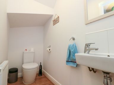A small bathroom with a toilet, a sink with a faucet, a blue towel on a ring, a mirror, a trash bin, and a toilet brush at Dotty's Sunshine Cottage The Bay near Filey