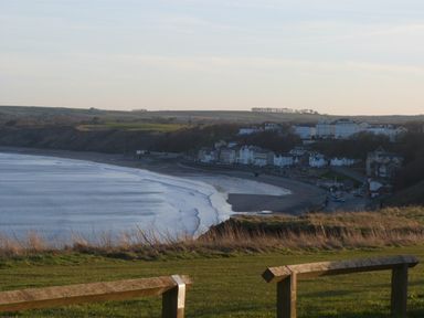A coastal view with waves washing onto a beach and buildings along the shoreline at Dotty's Sunshine Cottage in The Bay near Filey