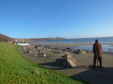 A beachside promenade with a metal statue, mini golf course, and sea cliffs at Dotty's Sunshine Cottage in The Bay near Filey