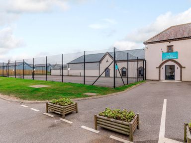 An outdoor view of The Bay Leisure Centre with paved parking area and fenced sports court at The Bay near Filey