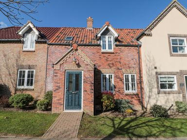 A brick house with a blue front door and windows with white frames surrounded by shrubs at Dotty's Sunshine Cottage The Bay near Filey