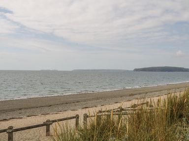 A beach with sand and grass near the shore and the sea with distant land in the background at Wavecrest in Pwllheli