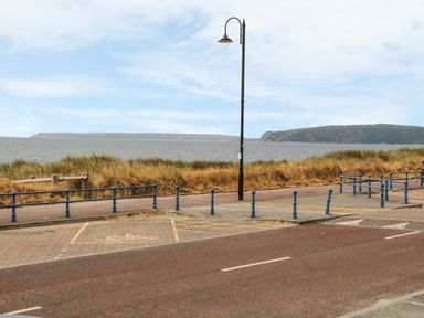A coastal road with a street lamp blue railings and ocean in the background at Wavecrest in Pwllheli