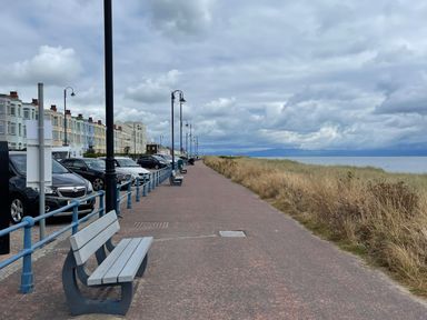 A coastal promenade with benches and parked cars beside pastel-colored buildings near the sea at Wavecrest in Pwllheli
