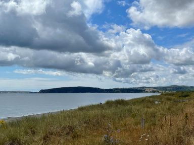 A coastal landscape with grassy dunes and a body of water under a cloudy sky at Wavecrest in Pwllheli