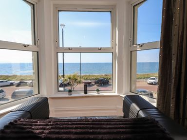 A living room with a view of the sea and parked cars at Wavecrest in Pwllheli