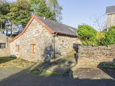A stone house with small windows and a tiled roof next to a stone wall with bushes at Yr Hen Dy in Llan Ffestiniog
