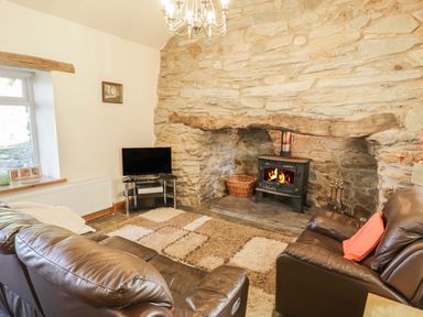 A living room with leather sofas a wood stove in a stone fireplace and a television at Yr Hen Dy in Llan Ffestiniog