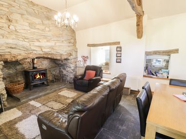 A living room with a stone fireplace wood stove leather sofa and armchair a wooden dining table and chairs at Yr Hen Dy in Llan Ffestiniog