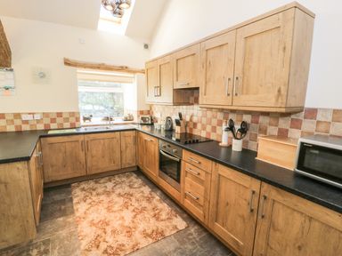 A kitchen with wooden cabinets and black countertops with a window above the sink at Yr Hen Dy in Llan Ffestiniog