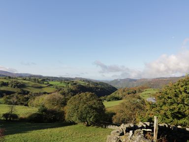 A landscape with rolling green hills trees stone fence and distant mountains at Yr Hen Dy in Llan Ffestiniog
