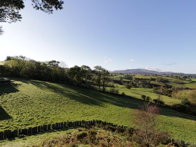 A rural landscape with green fields trees and hills under a clear sky at Yr Hen Dy in Llan Ffestiniog