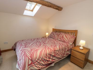A bedroom with a bed with red and white patterned bedding two bedside tables with lamps and a skylight window at Yr Hen Dy in Llan Ffestiniog