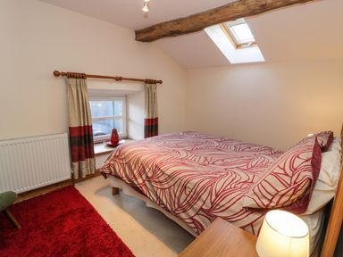 A bedroom with a double bed red patterned bedding a wooden bedside table lamp a window with curtains a skylight and a red rug on the floor at Yr Hen Dy in Llan Ffestiniog