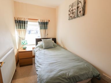A small bedroom with a single bed a pillow a bedside table with a lamp a window with curtains and a radiator at Yr Hen Dy in Llan Ffestiniog