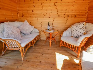 A wooden room with wicker furniture including a loveseat and two armchairs and a small round table with a bottle and glasses at The Flat At Brwyn in Brynford