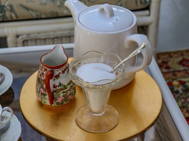 A white teapot, a patterned creamer jug, and a glass sugar bowl with a spoon on a round gold tray at The Flat At Brwyn in Brynford