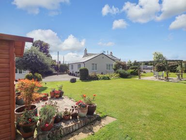 A garden with potted plants a white house and a patio with chairs and table at The Flat At Brwyn in Brynford