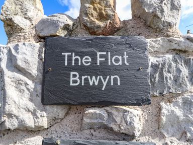 A stone wall with a dark plaque reading The Flat Brwyn at The Flat At Brwyn in Brynford
