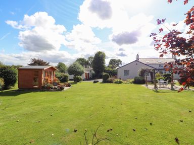 A grassy garden with a wooden shed flower pots and a patio with chairs and a table at The Flat At Brwyn in Brynford