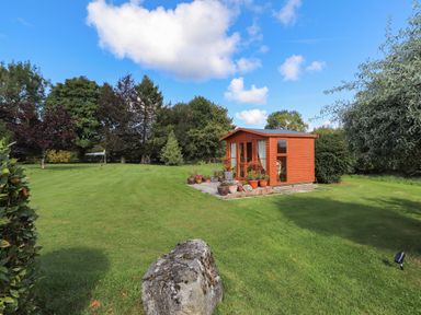 A garden with a small wooden shed surrounded by potted plants and trees at The Flat At Brwyn in Brynford