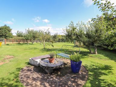 An outdoor garden area with a circular patio table plants a metal bench and trees at The Flat At Brwyn in Brynford