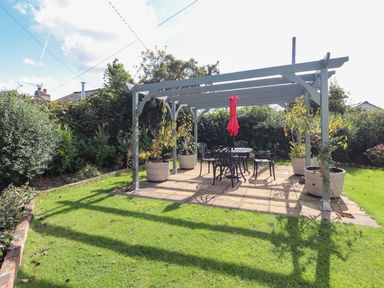 A garden with a pergola and outdoor dining set on a paved area at The Flat At Brwyn in Brynford