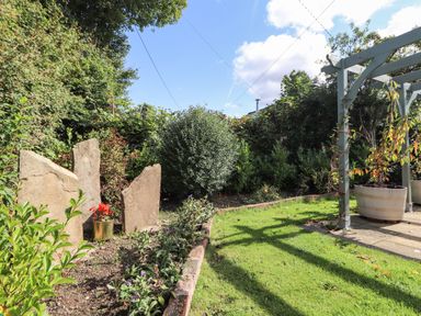 A garden with a grass lawn stone slabs flower beds and a wooden pergola at The Flat At Brwyn in Brynford