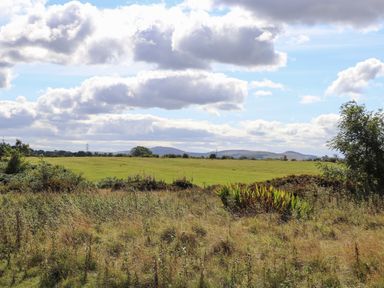 An open field with grass and shrubs under a cloudy sky at The Flat At Brwyn in Brynford