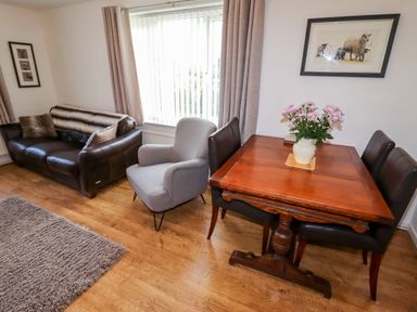 A living room with a brown leather sofa gray armchair wooden dining table with flowers and black chairs at The Flat At Brwyn in Brynford